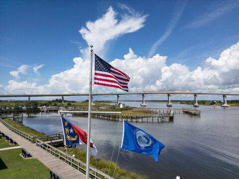 Aerial view of the American, North Carolina, and Town of Topsail Beach flags flying on a pole with a bridge spanning the sound in Topsail Beach, North Carolina, United States.