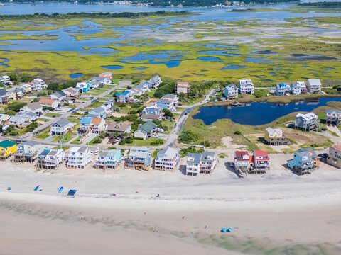 Aerial view of colorful beach houses lining the sandy shore with marshlands and tidal pools in the background in North Topsail Beach, North Carolina, United States.