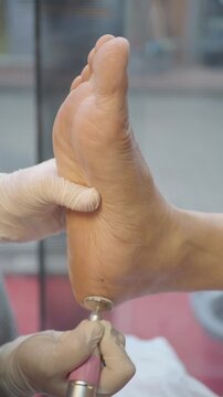 Professional podiatrist using electric foot file to remove dead skin and calluses from heel during pedicure procedure