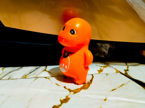 Orange dinosaur toy stands on marble surface