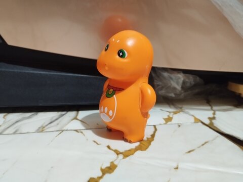 Orange dinosaur toy stands on marble surface