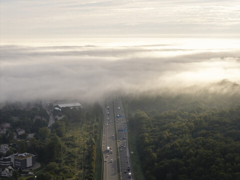 Aerial view of a highway cutting through a dense forest with thick morning fog rolling over the landscape in Krakow, Lesser Poland Voivode, Poland.
