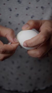 Close up view of hands peeling hard boiled white egg shell showing cooking preparation process