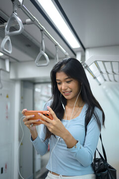 Young Asian Woman Using Smartphone with Earphones on Subway Train