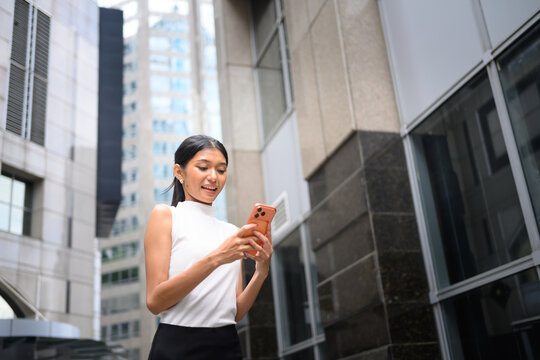 Young Businesswoman Walking Outdoors in City District While Reading Smartphone with Surprised Expression