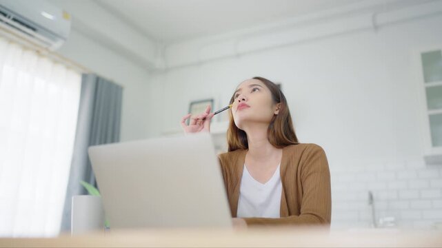 Beautiful young Asian woman working with laptop computer in home kitchen. Work at home