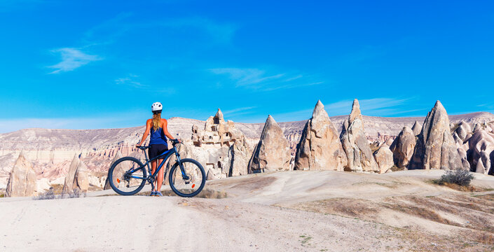 Woman cyclist with mountain bike looking at rock formations in Goreme valley Cappadocia Turkey