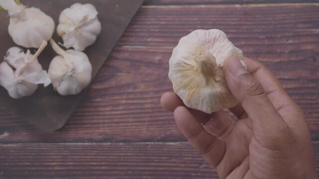 Close-up of hand turning a fresh garlic bulb over wooden table, food ingredient