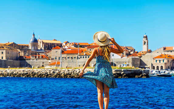 Happy woman wearing summer dress and hat looking at old town Dubrovnik Croatia from sea