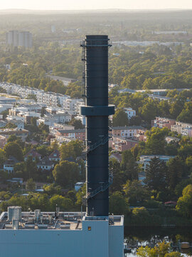 Aerial view of the Lichterfelde power plant chimney rising above residential buildings and lush green trees in the urban landscape of Berlin, Berlin, Germany.