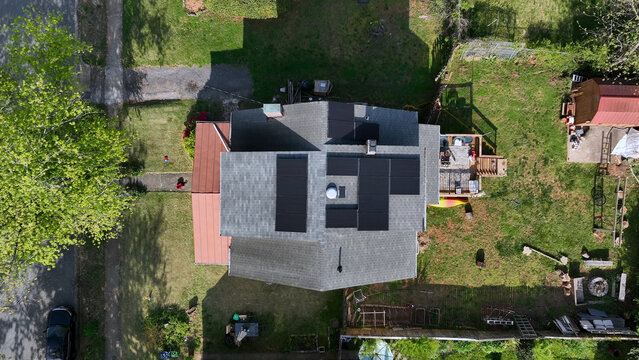 Aerial view of a residential house featuring modern solar panels on the roof, surrounded by a green lawn, mature trees, and a backyard deck in Lynchburg, Virginia, United States.