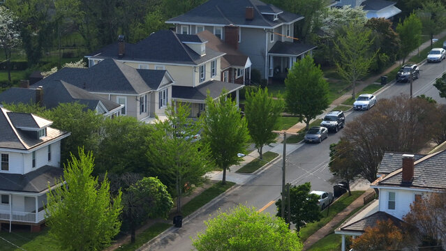 Aerial view of a quiet residential street lined with historic houses, lush green trees, and parked cars in Lynchburg, Virginia, United States.