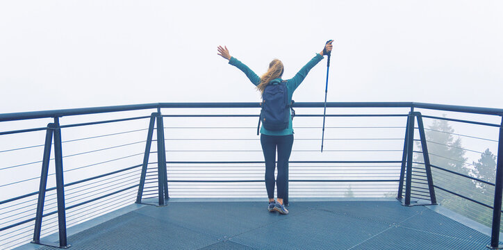 Hiker woman standing with arms raised on foggy mountain viewpoint enjoying freedom