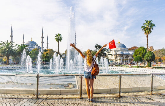 Happy tourist woman holding turkish flag in front of Sultanahmet Mosque and fountain in Istanbul