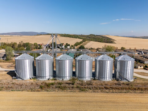 Aerial view of grain silos and agricultural storage facility in Paszto, Nograd County, Hungary, surrounded by summer farmland and crop fields under a clear sky.