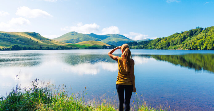 Woman standing by a mountain lake looking into the distance during summer adventure
