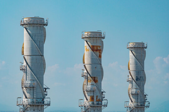 Aerial view of three distinctive exhaust stacks rising above a modern combined cycle power plant under a clear blue sky in Chivasso, Piedmont, Italy.