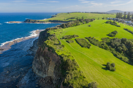 Aerial view of a loping green hillside leading up to a tall sea cliff