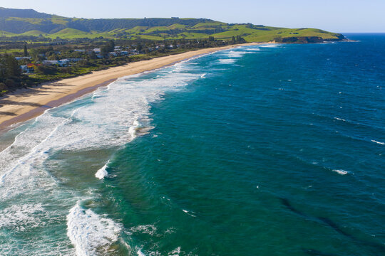 Aerial view of waves crashing on to a long sandy beach leading to a coastal headland