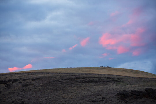 Dramatic pink sunset clouds over a rolling hill