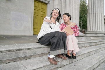 Obraz premium Young women friends sitting on stone stairs talking