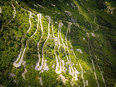Aerial view of the famous serpentine road winding through the steep mountain slopes with lush green vegetation under bright sunlight in Kotor, Kotor Municipality, Montenegro.