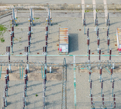 Aerial view of high voltage switchgear and electrical substation infrastructure at a power generation facility with metal structures and gravel ground in Italy.