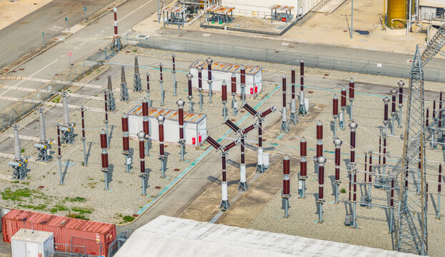 Aerial view of a high voltage electrical substation with circuit breakers, insulators and transmission equipment at an industrial power facility in Italy.