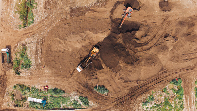 Aerial view of construction site with excavators and trucks working on brown earth in Chennai, India.