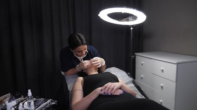 A close-up cosmetologist applies a contour to the lips with a brush before permanent makeup. The cosmetologist is preparing for the permanent makeup procedure.