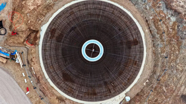 Aerial view of a circular wind turbine foundation featuring intricate steel rebar reinforcement patterns at a construction site in Latvia.