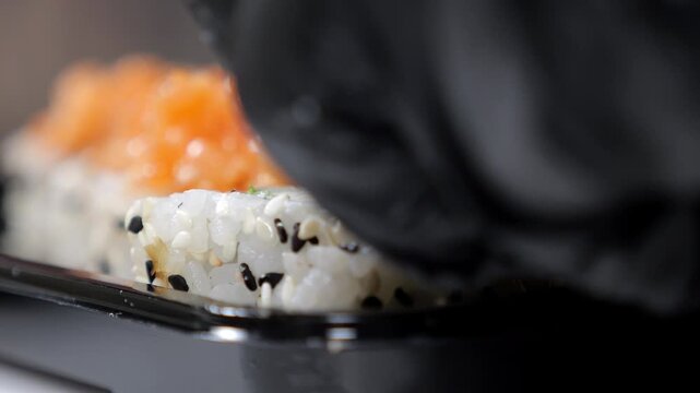 Close-up of a chef wearing gloves putting sliced salmon on sushi before baking, cooking baked sushi in the kitchen of a Japanese restaurant.