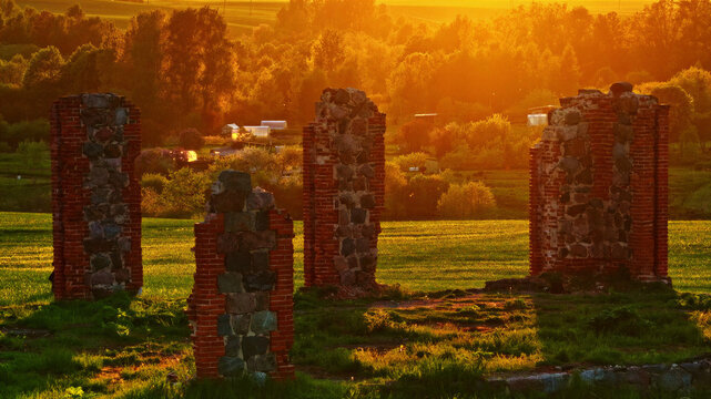 Aerial view of ancient stone and brick ruins standing in a grassy field during golden hour in Latvija.