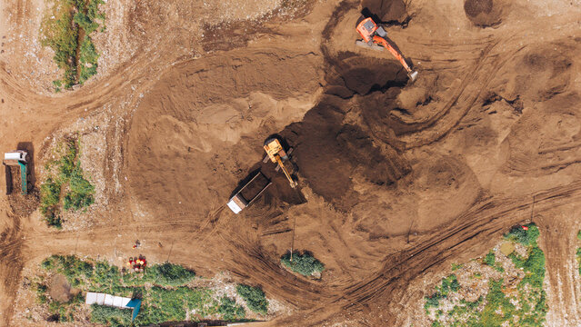Aerial view of excavators and dump trucks working on a construction site with piles of earth and tire tracks in Chennai, India.