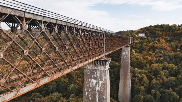 Aerial view of the historic Fades viaduct with its rusty iron truss structure and stone piers spanning over a dense forest in Les Ancizes-Comps, Auvergne-Rhone-Alpes, France.