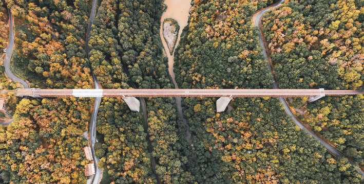 Aerial view of the historic Fades viaduct spanning the Sioule river, surrounded by dense autumn forests and winding roads in Les Ancizes-Comps, Auvergne-Rhone-Alpes, France.