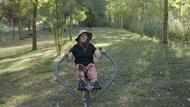Adult woman training using outdoor fitness equipment in a public park, focusing on physical health and active lifestyle