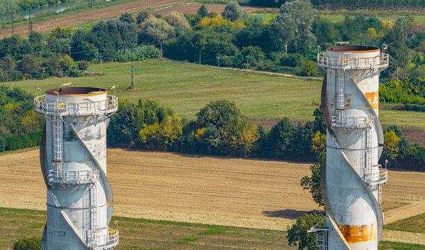 Aerial view of twin industrial exhaust stacks rising above farmland and rural landscape, highlighting large-scale energy infrastructure and power generation technology in Italy.