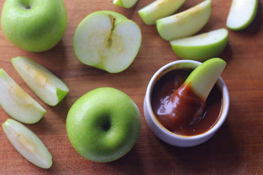 Green apples and fresh apple slices served with salted caramel dip for snacking on a wooden board