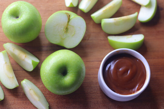 Green apples and fresh apple slices served with salted caramel dip for snacking on a wooden board