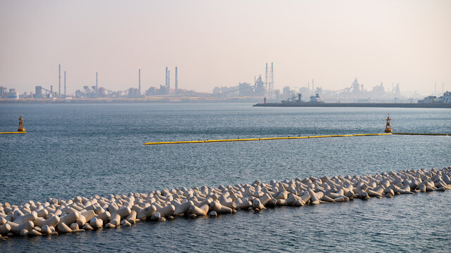 Aerial view of the industrial steelworks complex with chimneys and structures along the coastline, featuring concrete tetrapods in the foreground in Pohang-si, Gyeongsangbuk-do, South Korea.