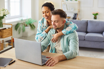 Obraz na płótnie Canvas Happy young mixed race at home office workplace using laptop computer for remote work, searching for information, giving each other advice, building relationship with mutual trust and support