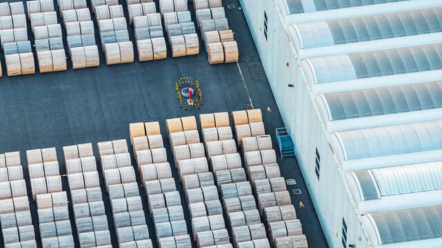 Aerial view of an industrial storage yard filled with large wooden cable reels beside a warehouse, highlighting logistics and manufacturing infrastructure in Italy.
