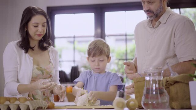 Caucasian family with parents teaching son kneading dough in kitchen