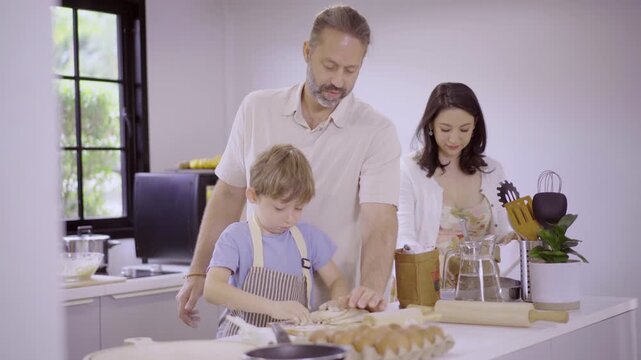 Caucasian family with parents teaching son kneading dough in kitchen
