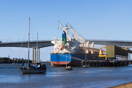 A bulk carrier ship docked at a loading facility on the Brisbane River near the Gateway Bridge