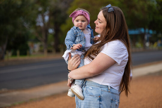 Mother cuddling toddler daughter outdoors in Australian neighbourhood