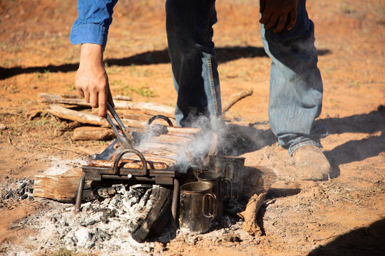 Sausages on a camping bbq over coals being turned with a pair of tongs