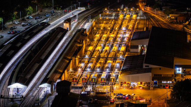 Aerial view of a train depot at night with multiple passenger trains parked on parallel tracks illuminated by bright overhead lights in Salisbury, Wiltshire, United Kingdom.