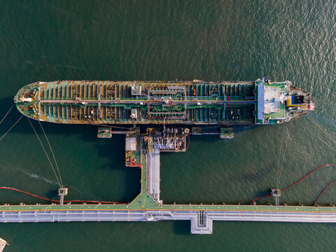 Aerial view of an oil tanker docked at a marine terminal with industrial piping and infrastructure in the sea in Cilacap Regency, Central Java, Indonesia.